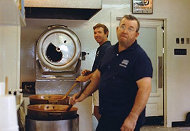 Everett Fisher and worker cooking up kettle corn in copper kettles in the kitchen